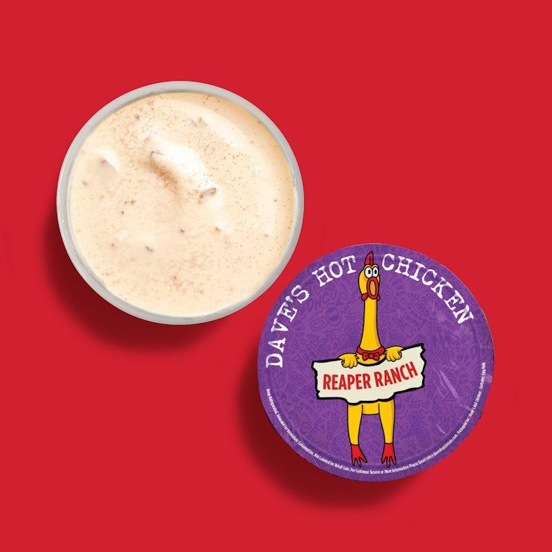 Top-down view of Dave’s Hot Chicken Reaper Ranch dipping sauce cup with purple branded lid on a red background.