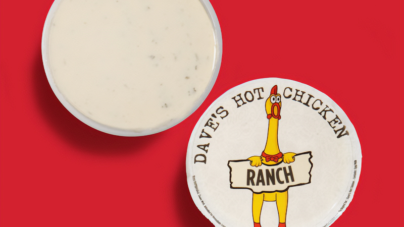 Top-down view of Dave’s Hot Chicken ranch dipping sauce cup with branded lid on a red background.