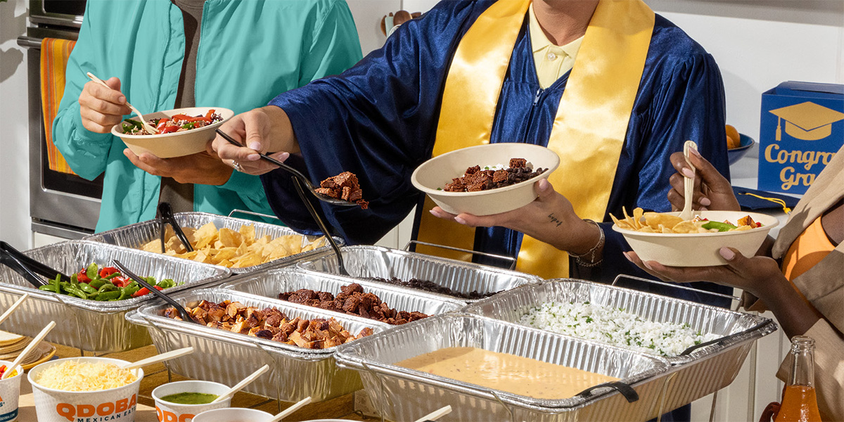 Graduation party guests build customizable QDOBA meals from a catering hot bar while celebrating a graduate in cap and gown at a graduation open house.