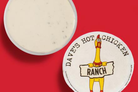 Top-down view of Dave’s Hot Chicken ranch dipping sauce cup with branded lid on a red background.