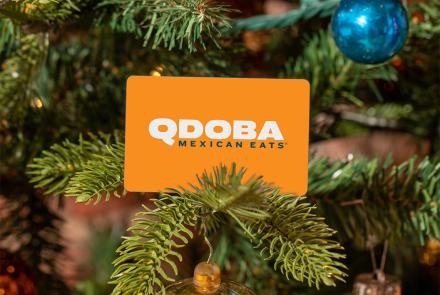 QDOBA Mexican Eats gift card hanging on a decorated Christmas tree branch with ornaments and holiday lights.
