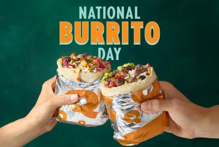 Two hands holding QDOBA burritos filled with steak, queso, guacamole, and fresh toppings under “National Burrito Day” text promoting a BOGO offer.